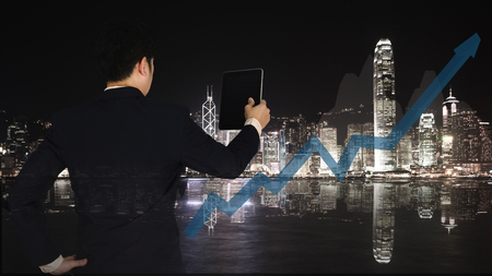 Double exposure of businessman using tablet to manage his business with financial graph chart and cityscape blurred building background. business vision conceptの写真素材