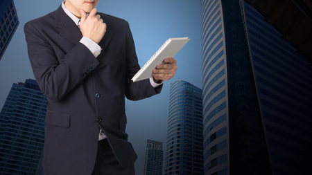 Double exposure Confident Asian businessman reading notebook or document file with cityscape on blurred building background, business concept,の写真素材