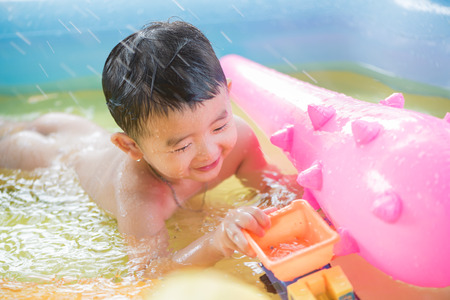 Asian kid playing in inflatable baby pool. Boy swim and splash in colorful swimming pool with water toys on hot summer day.の写真素材