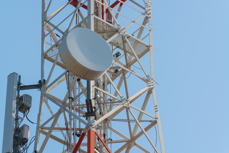 Mobile phone communication antenna tower with satellite dish on blue sky background,...