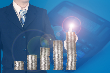 Double exposure businessman hand touching virtual panel of growth bar chart on financial graph chart with piles of coins arranged as a graph and calculator, business success concept.
の写真素材