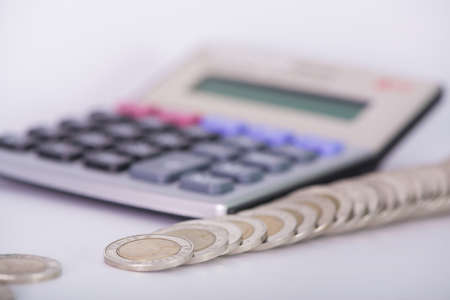 Stack of money in the form of coins and calculator on white background. saving concept. shallow focusの写真素材