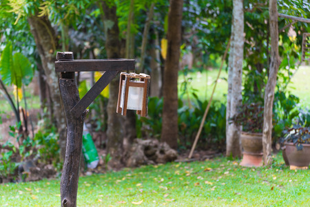 Old lamp on a short wooden pole with grass and tree in tropical garden.の写真素材