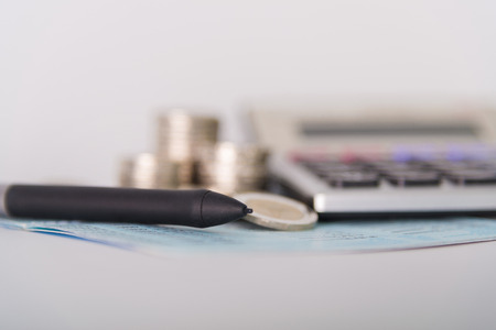 Savings, increasing columns of coins, piles of coins arranged as a graph and calculator with pen on white background, business idea, shallow focus.の写真素材