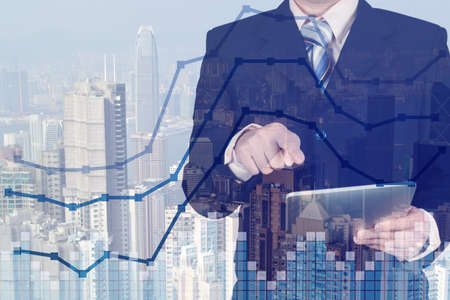 Double exposure businessman using tablet manage his business on stock market chart and city...