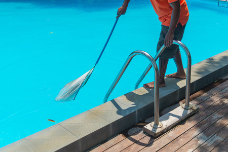 Man cleaning the blue swimming pool from leaves with cleaning net, Summer maintenance service.の写真素材