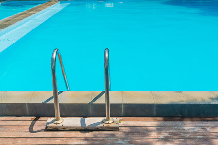 Swimming pool stair with wooden flooring in resort under sunlight.