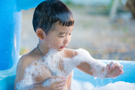Asian boy playing with water and foam in inflatable baby pool on hot summer day. shallow focus.の写真素材