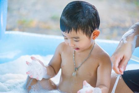 Asian boy playing with water and foam in inflatable baby pool on hot summer day. shallow focus.の写真素材