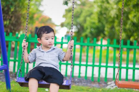 Young Asian boy play a iron swinging at the playground under the sunlight in summer, Kids play on school yard. Happy kid in kindergarten or preschool. Children having fun at daycare play ground.の写真素材