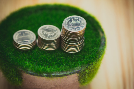 Stack of gold coin  on artificial grass in pot, on wooden table with green nature background in vintage tone. shallow focus. business success and banking concept.の写真素材