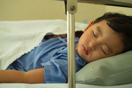 Sick Asian kid boy 2 years old lying sick in hospital bed. dim light, selective focus.の写真素材