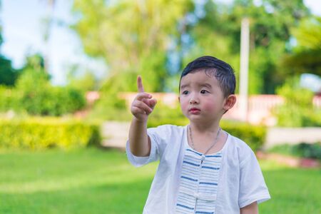 Asian little Kid pointing up by fingers to something or empty copy space under sun light outdoor in...
