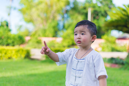 Asian little Kid pointing up by fingers to something or empty copy space under sun light outdoor in the garden.の写真素材