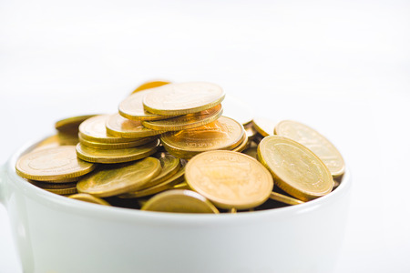 Golden coins in a white cup  of coffee on the white background, saving money concept.の写真素材