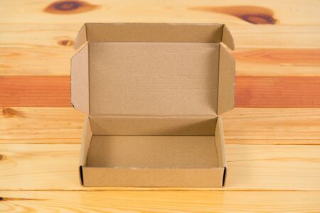 Empty brown cardboard box for mock up on bright wooden table with copy space.