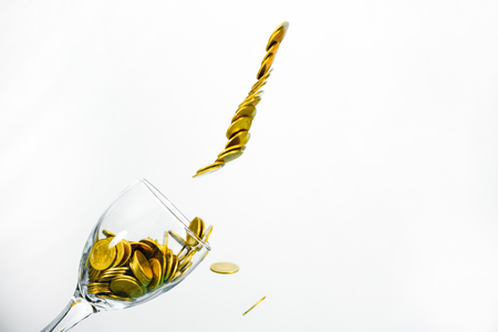 Golden coins splash in a glass of champagne on the wall background with copy space., saving money concept.の写真素材