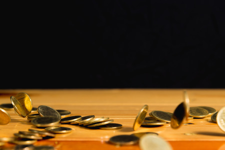 Falling gold coins money on wooden table with black wall, copy space, business wealth concept. thin...