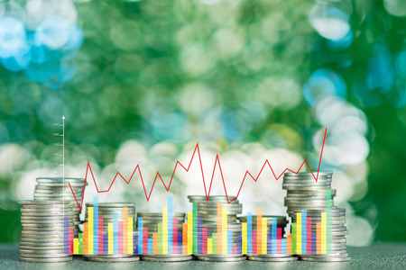 Double exposure of stacks of coins on the table in garden with financial graph chart, finance...