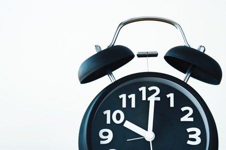 Close up of black color vintage alarm clock on white wall, wake up time concept