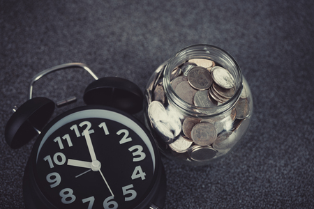 Alarm clock and step of coins stacks with coin in glass jar on working table, time for savings money concept, banking and business idea. vintage tone.の写真素材