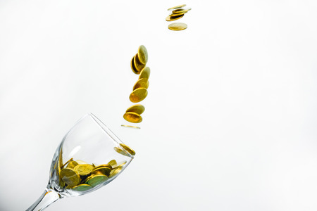Golden coins splash in a glass of champagne on the wall background with copy space., saving money concept.の写真素材