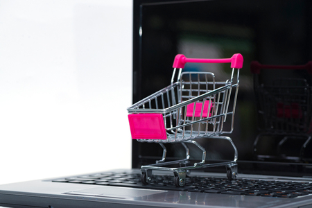 Shopping cart or supermarket trolley with laptop notebook on white background and copy space, e-commerce and online shopping concept.の写真素材