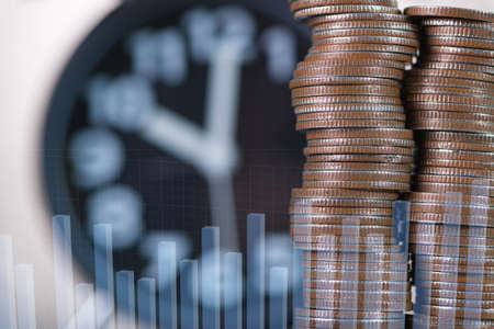 Double exposure of alarm clock and piles of coin with financial graph, time for savings money concept, banking and business idea.の写真素材