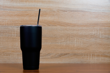 Black colour stainless steel tumbler or cold storage cup with water straw and cap on wooden background.の写真素材