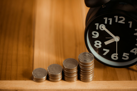 Alarm clock and step of coins stacks on working table, time for savings money concept, banking and business idea. vintage tone.の写真素材