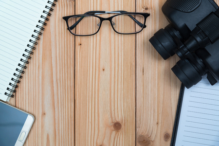 Essential vacation items, sneakers, glasses, smart phone, binocular, notebook and pen on wooden floor ready to travel, top view with copy space, Travel and vacation concept.の写真素材