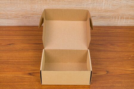 Empty opened brown cardboard box or tray for mock up on bright wooden table with copy space.