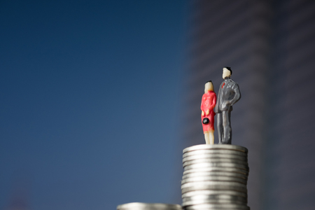 Figure miniature businessman of small people investor and office worker secretary standing on stack of coin, with modern city background for money and financial business success concept.の写真素材
