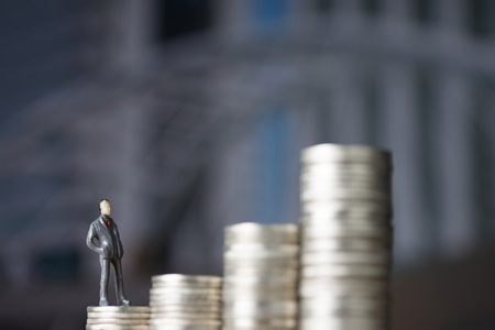 Figure miniature businessman of small people standing on first step of coin stack and look at the top of coin, with modern city background for money and financial business challenge concept.の写真素材