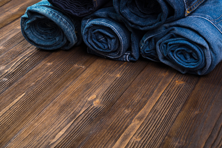 Roll Frayed jeans or blue jeans denim collection on rough dark wooden table background with copy space, old fashion style concept.の写真素材