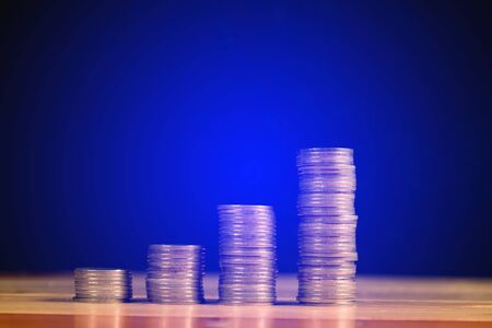 Savings, increasing columns of gold coins, piles of gold coins arranged as a graph on wooden table with black wall, business banking idea, shallow focus. soft tone.の写真素材