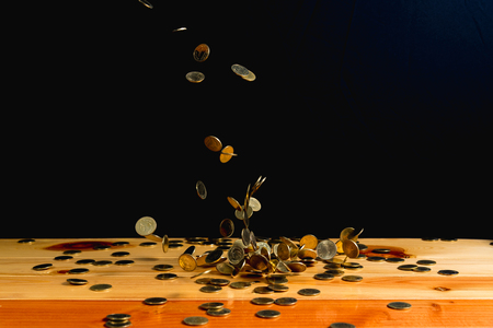 Falling gold coins money on wooden table with black wall, copy space, business wealth concept. thin focusの写真素材