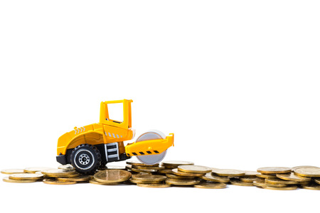 Mini Road roller machine with stack coin with pile of gold coin, isolated on white background with copy space, business finance and banking industrial concept idea.の写真素材