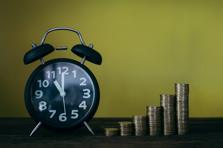Alarm clock and step of coins stacks on working table, time for savings money concept, banking and business idea.の写真素材