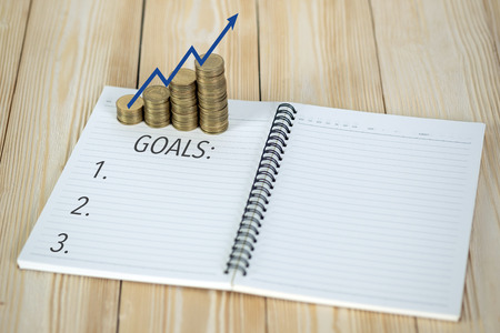 Steps of coins stack with notebook paper on wooden working table with copy space for text, financial and business planning concept idea.の写真素材