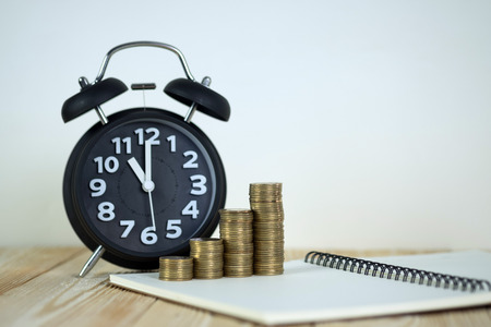 Steps of coins stack with vintage alarm clock and pen, notebook paper on wooden working table with...