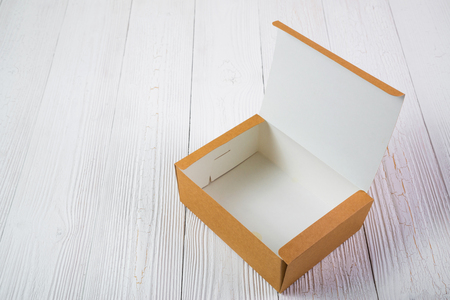 Empty Package brown cardboard box or tray on bright white wooden table with copy space.
