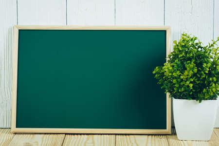 Blank green chalkborad with wood frame and little decorative tree in white vase on wooden table with copy space for add text.の写真素材