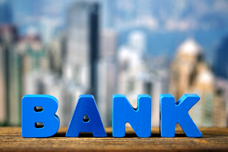 BANK text on top wooden working table with city and office building background, business and financial concept idea.の写真素材