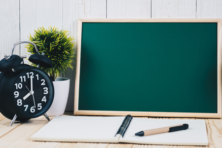 Blank green chalkborad and little tree with vintage alarm clock and notebook paper pen on wooden table with copy space for add text.の写真素材