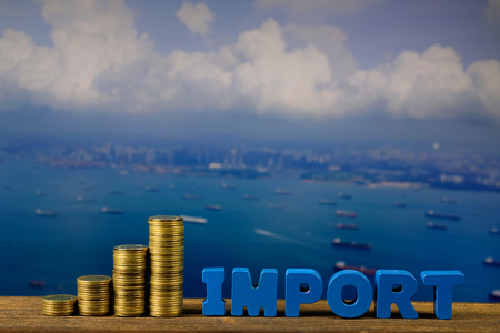 IMPORT text and stack of coin on wood table over seascape and cargo ship view from aerial, import...