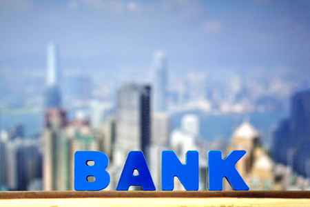 BANK text on top wooden working table with city and office building background, business and financial concept idea.の写真素材