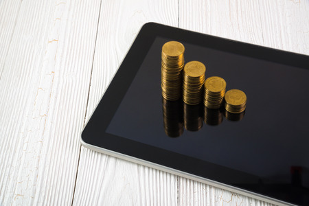 Step of coin stack on tablet computer screen on white working table, business and finance concept idea.の写真素材