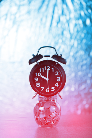 Alarm clock and step of coins stacks with coin in glass jar on working table, time for savings money concept, banking and business idea.の写真素材