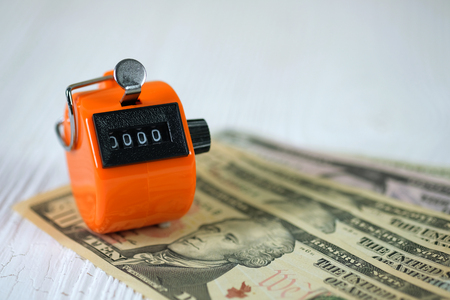 Tally counter or counting machine with 0000 number, coin and banknote on white wooden table,...